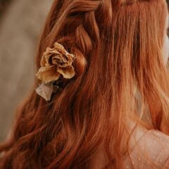 Vrouw met koperrood haar in een vlecht met een gedroogde bloem, warme natuurlijke rode haarkleur
