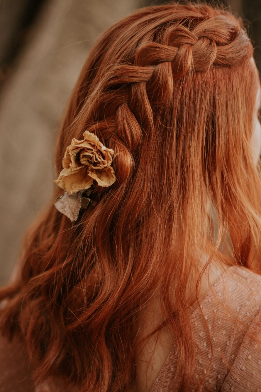 Vrouw met koperrood haar in een vlecht met een gedroogde bloem, warme natuurlijke rode haarkleur