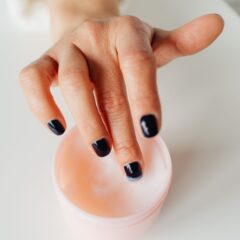 Vrouw schept met haar vinger handcrème uit een potje om haar droge handen in te smeren