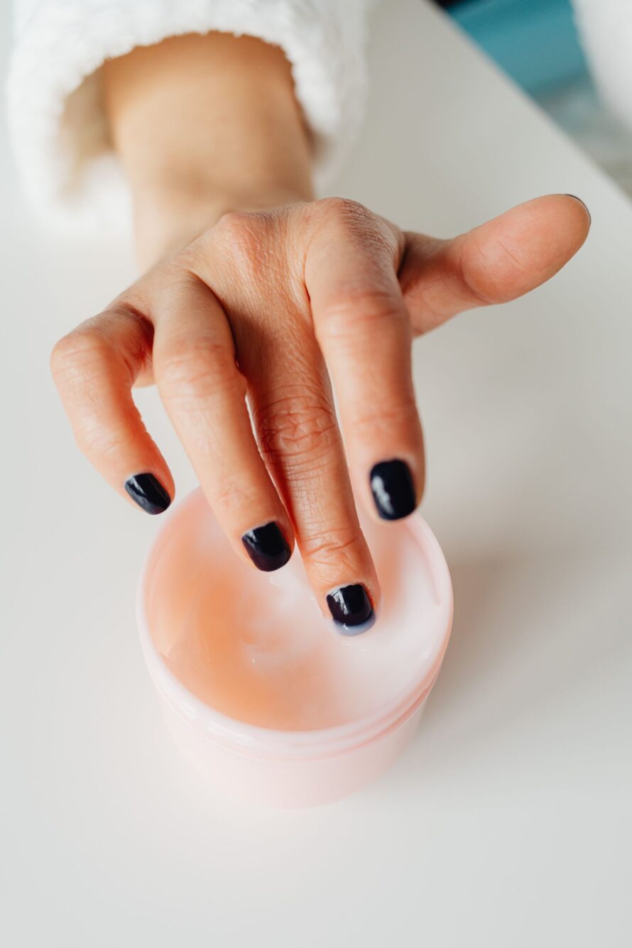 Vrouw schept met haar vinger handcrème uit een potje om haar droge handen in te smeren